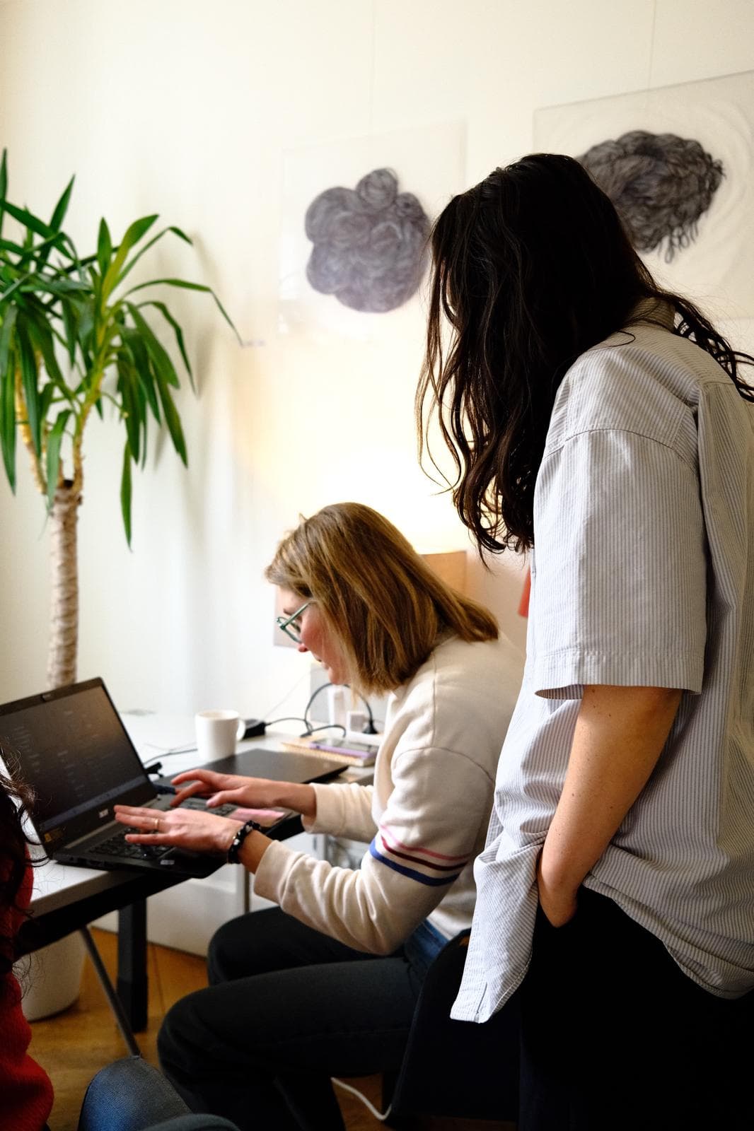 Deux femmes travaillent ensemble sur un ordinateur portable, une troisième les observe.