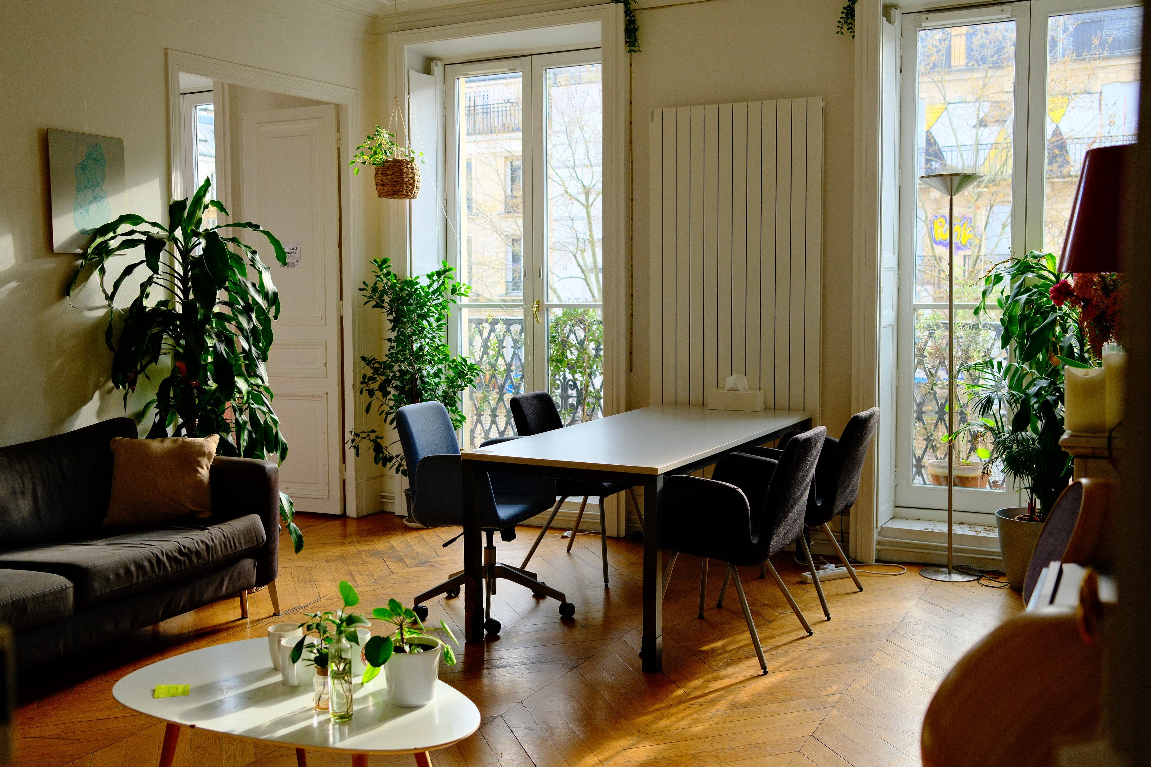 Salle de travail lumineuse du Base Camp : grande table, chaises, plantes et fenêtres donnant sur Paris.