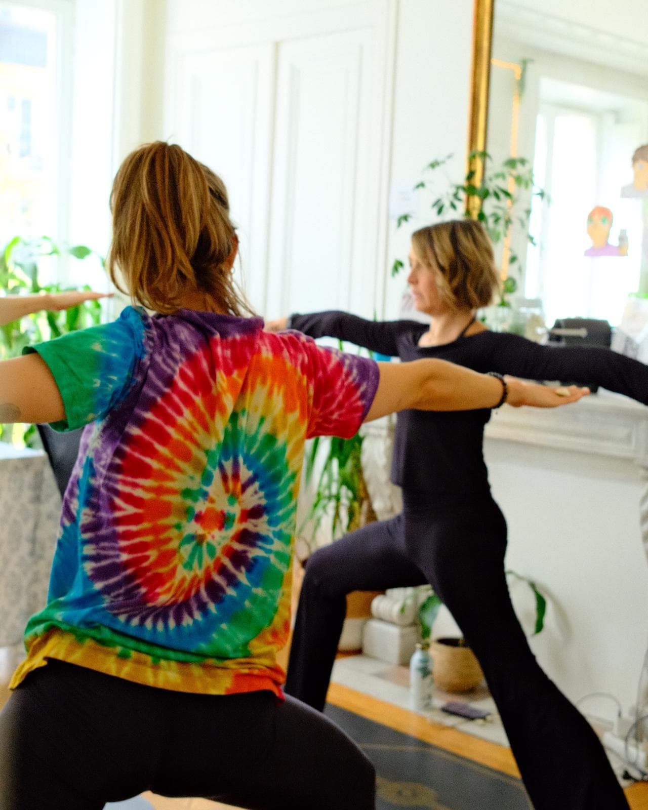 Deux femmes enchaînent une posture de yoga guerrier dans le salon baigné de lumière.